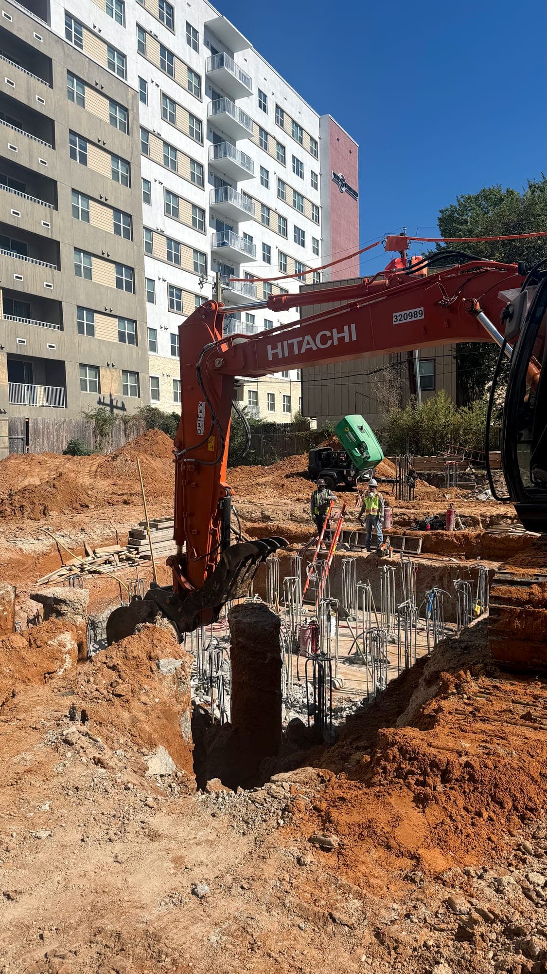 Excavator working alongside pier reinforcement on a multi-story site