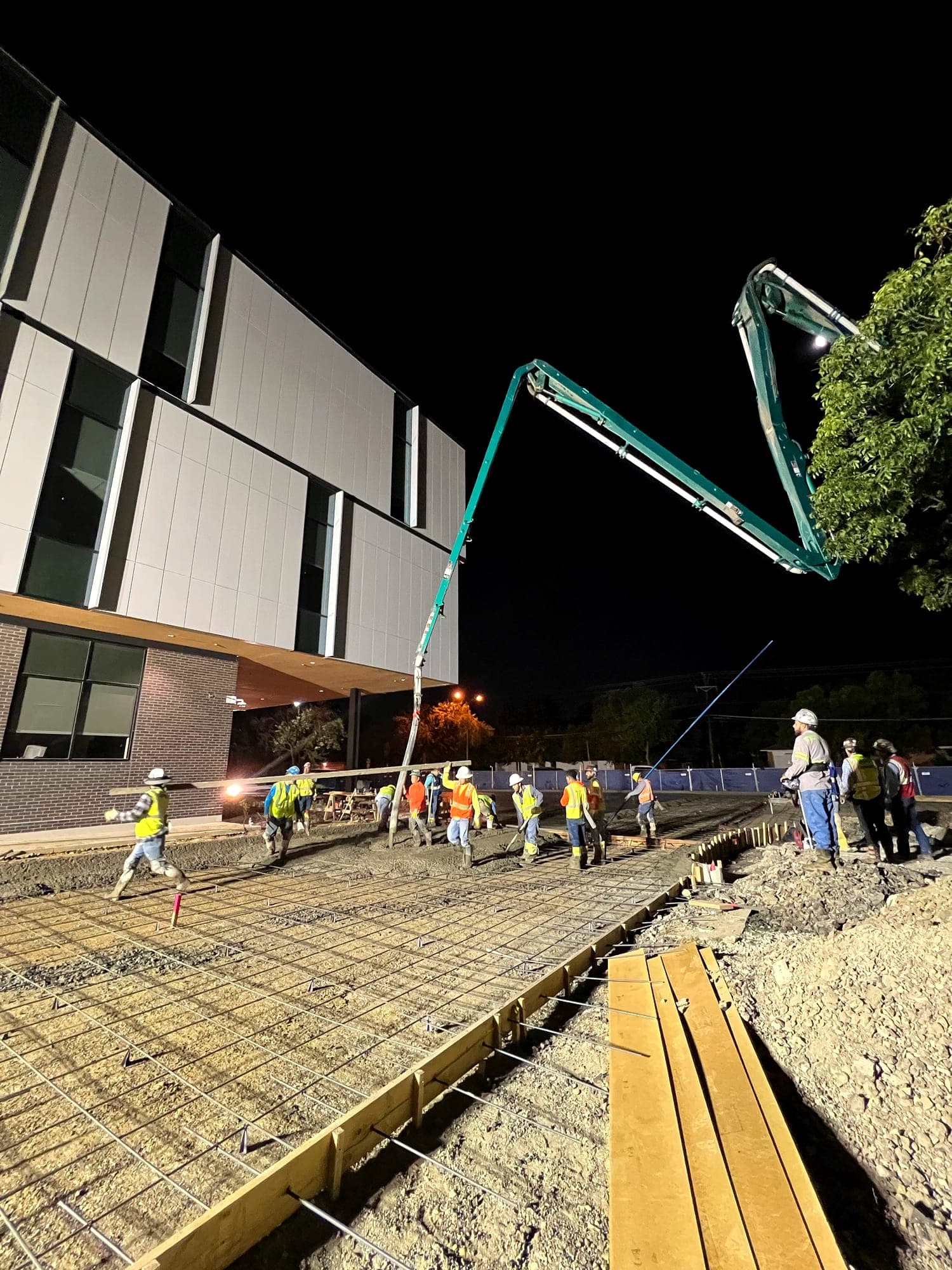 Concrete pump boom reaching across a building site during a night placement