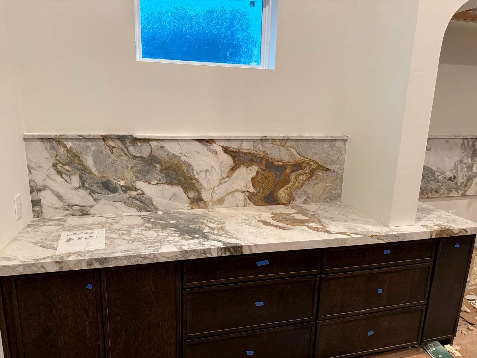 Stone counters and matching backsplash installed over dark cabinetry