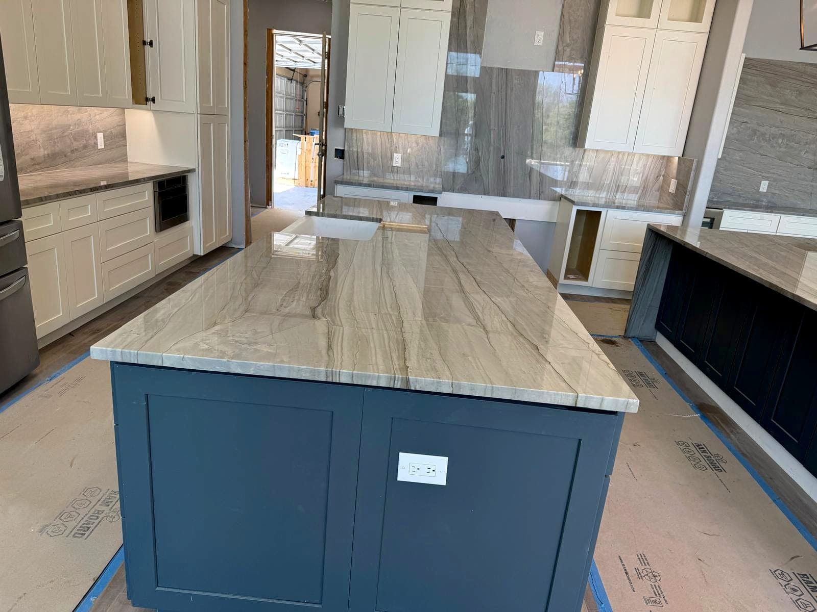 Quartzite island top and full-height backsplash installed on two-tone cabinetry
