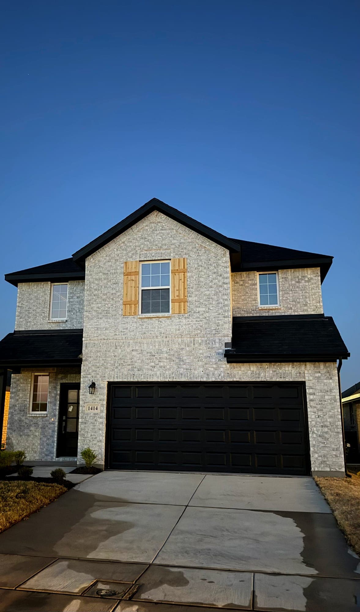 Completed two-story elevation in light brick with black trim, board-and-batten shutters and a finished driveway