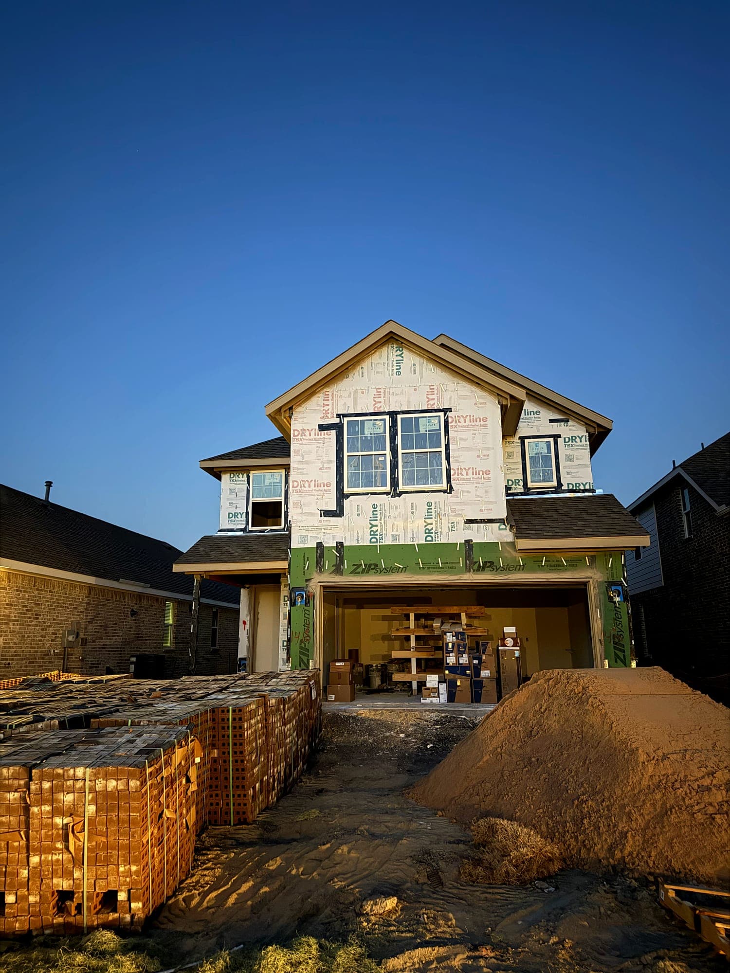 Two-story home dried in with house wrap and sheathing tape, brick banded on pallets in the drive ready to lay
