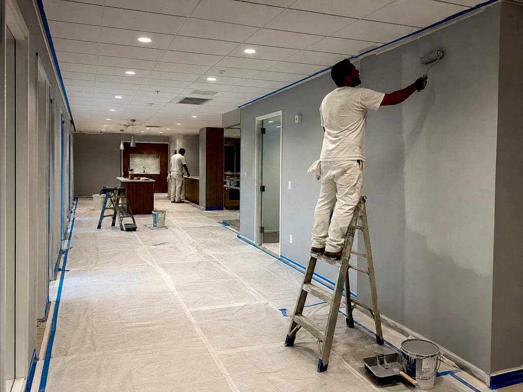 Painter cutting in along a commercial corridor with taped edges and covered floors