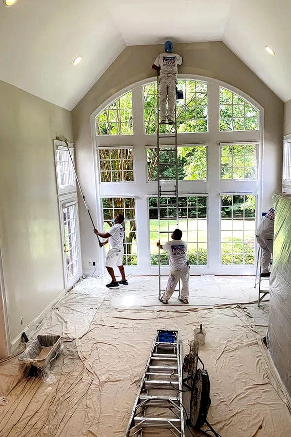 Painting crew coating walls around a tall arched window with floors and openings masked